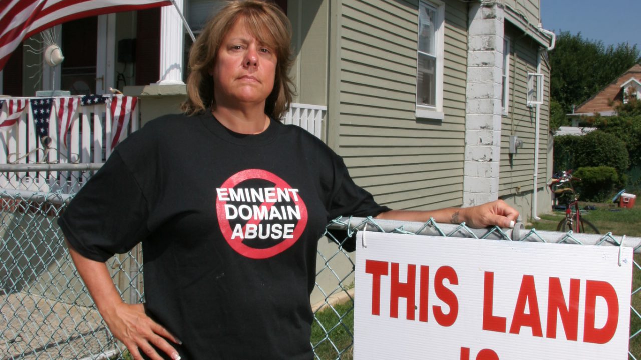 Woman standing in front of her house in Long Beach New Jersey with a sign that says This Land is My Land