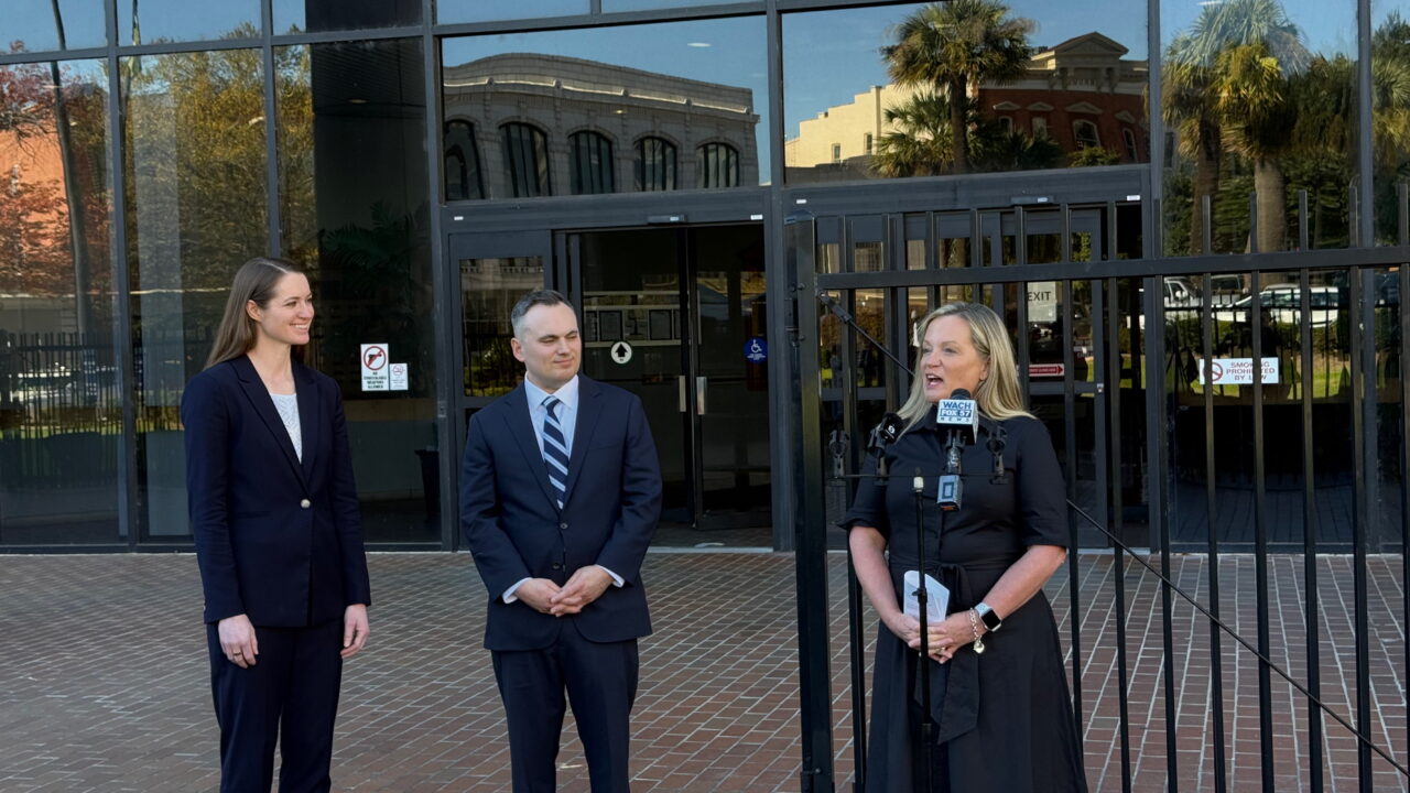 Renee Flaherty speaks at outdoor microphones beside two attorneys during a South Carolina press conference