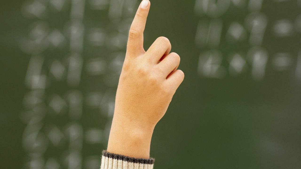 Close-up of girl's hand raised in classroom (10-11)