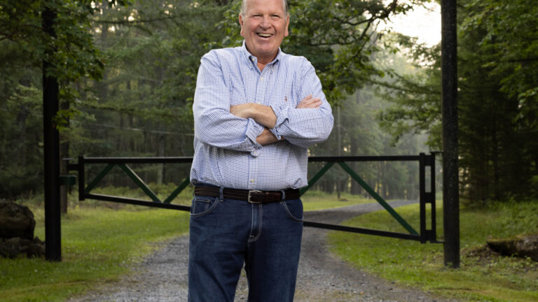 Frank Stockdale smiling with arms crossed on a gravel driveway near a gate in Pennsylvania