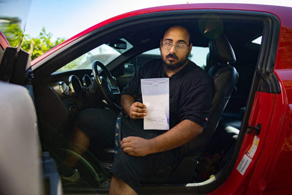 man sitting in car holding traffic ticket