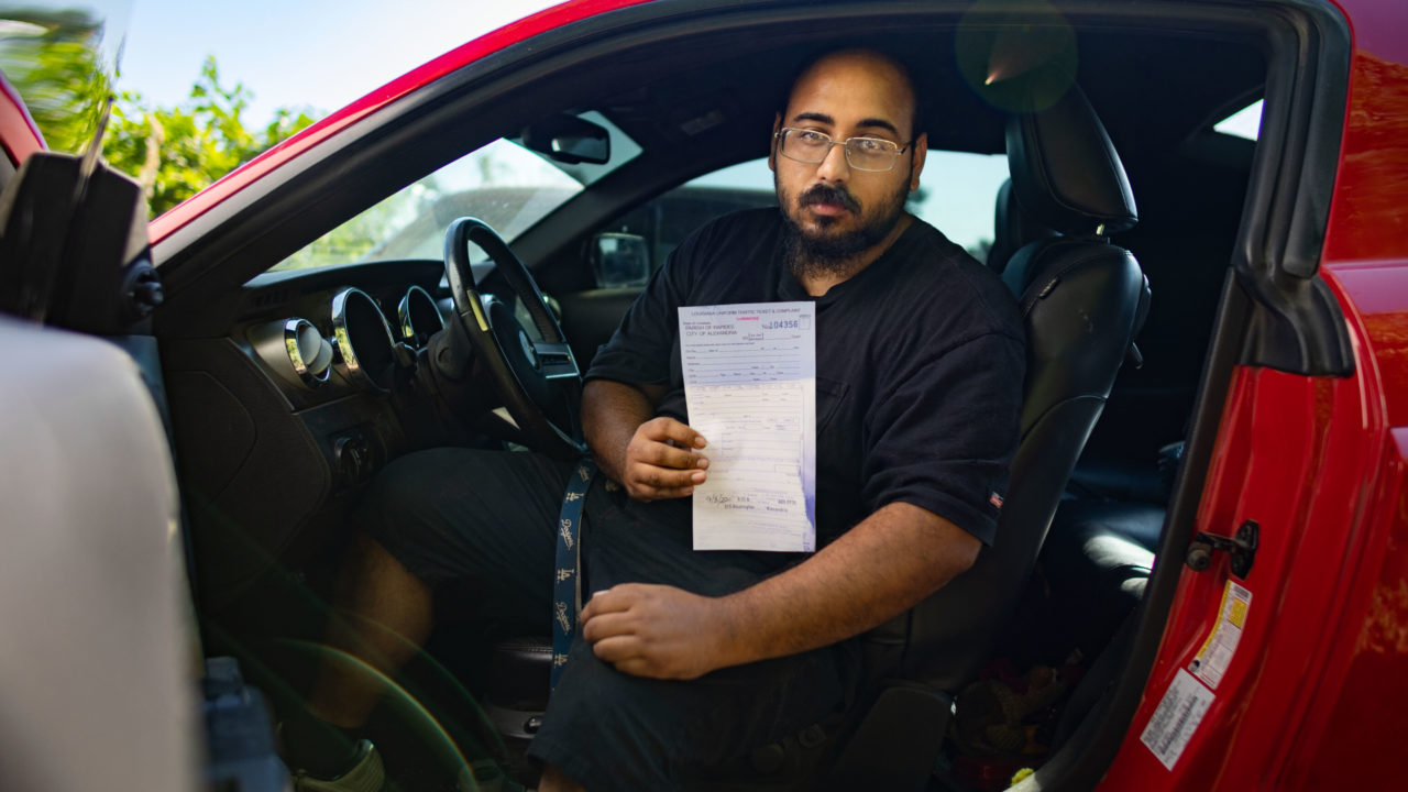 man sitting in car holding traffic ticket