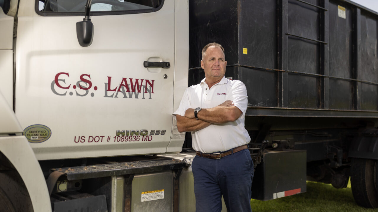 man stands in front of lawn care equipment and dump truck