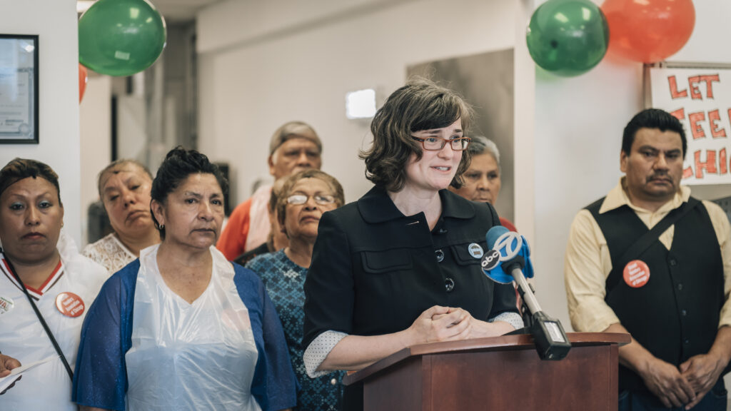 Beth Kregor speaks at a podium surrounded by street vendors at a Chicago press conference
