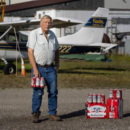 Ken Jouppi holds Budweiser cans near a small airplane on a grassy airstrip