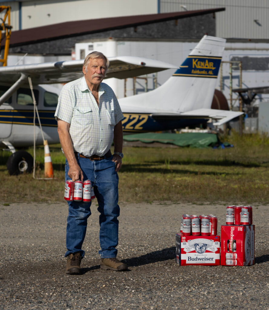 Ken Jouppi holds Budweiser cans near a small airplane on a grassy airstrip