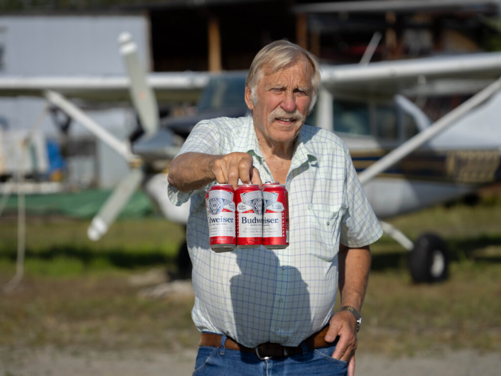 Ken Jouppi holds a six-pack of Budweiser near a small plane outdoors