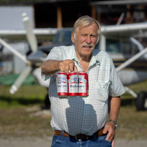 Ken Jouppi holds a six-pack of Budweiser near a small plane outdoors