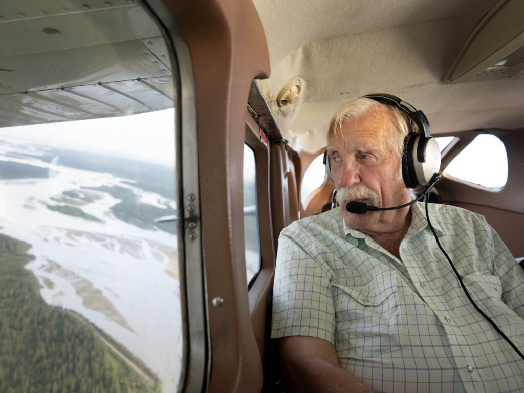 Ken Jouppi wearing a headset, looking out a small plane window over an Alaska river