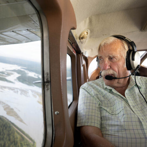 Ken Jouppi wearing a headset, looking out a small plane window over an Alaska river