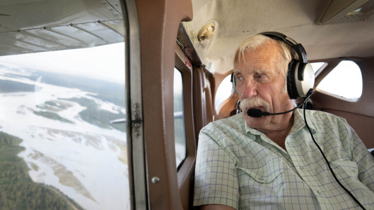 Ken Jouppi wearing a headset, looking out a small plane window over an Alaska river