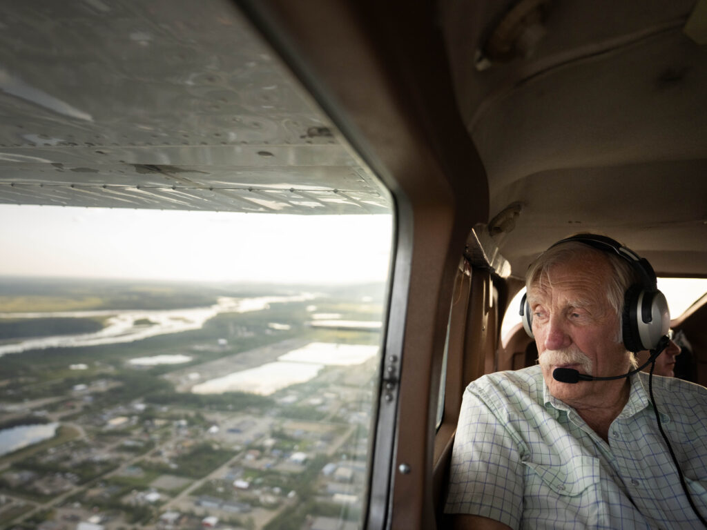 Ken Jouppi wearing headset looks out plane window over Alaska river and landscape below
