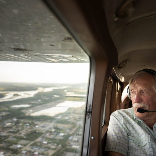 Ken Jouppi wearing headset looks out plane window over Alaska river and landscape below