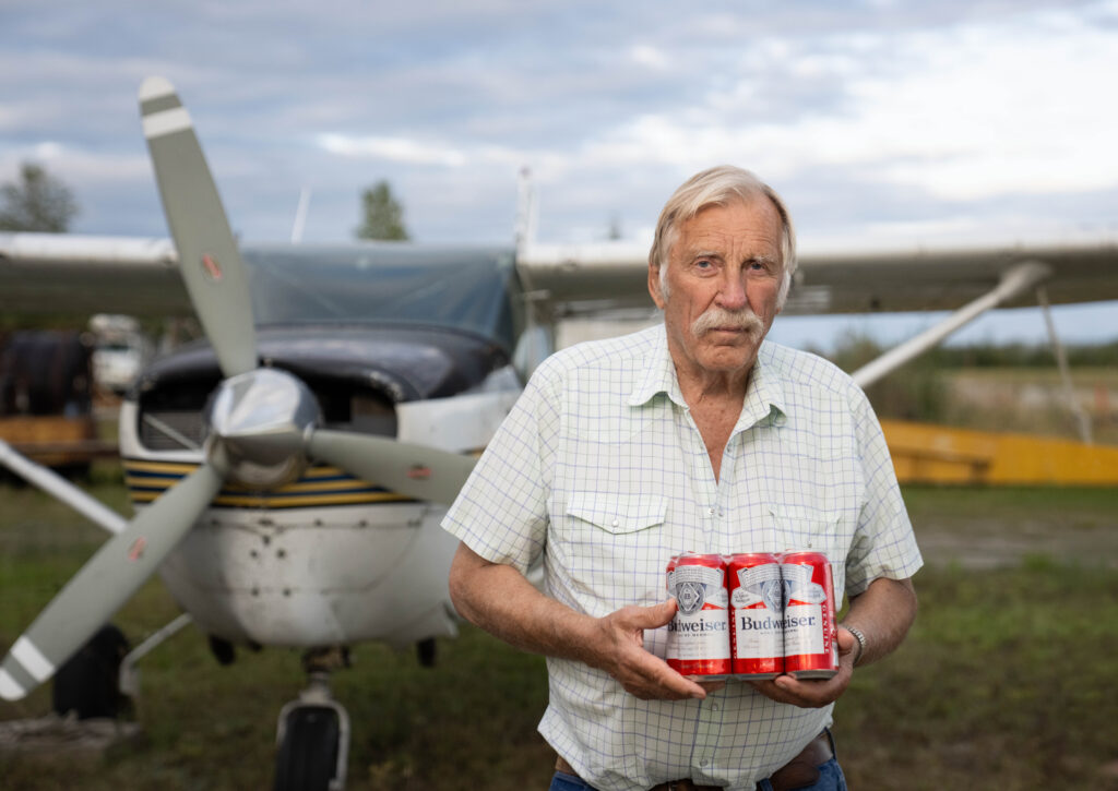 Ken Jouppi holds a six-pack of beer beside his small airplane outdoors