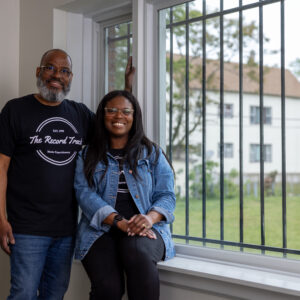 Man and woman wearing Record Track shirts smile by a barred window inside a building