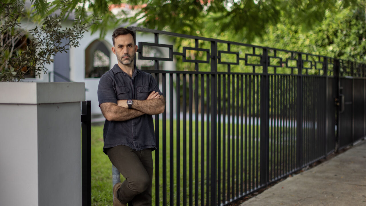 Chad Trausch stands arms crossed by his home's iron fence in Miami