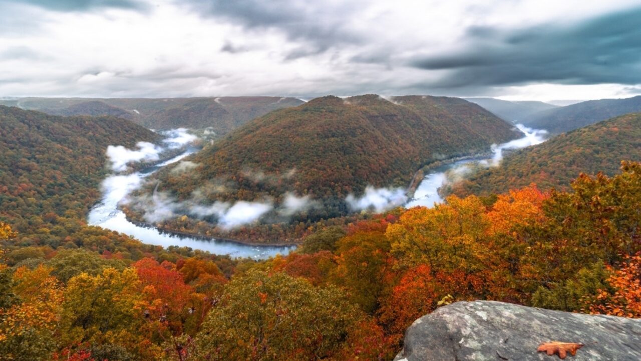 A river winding in a horseshoe bend through forested hills with autumn foliage under a cloudy sky in West Virginia