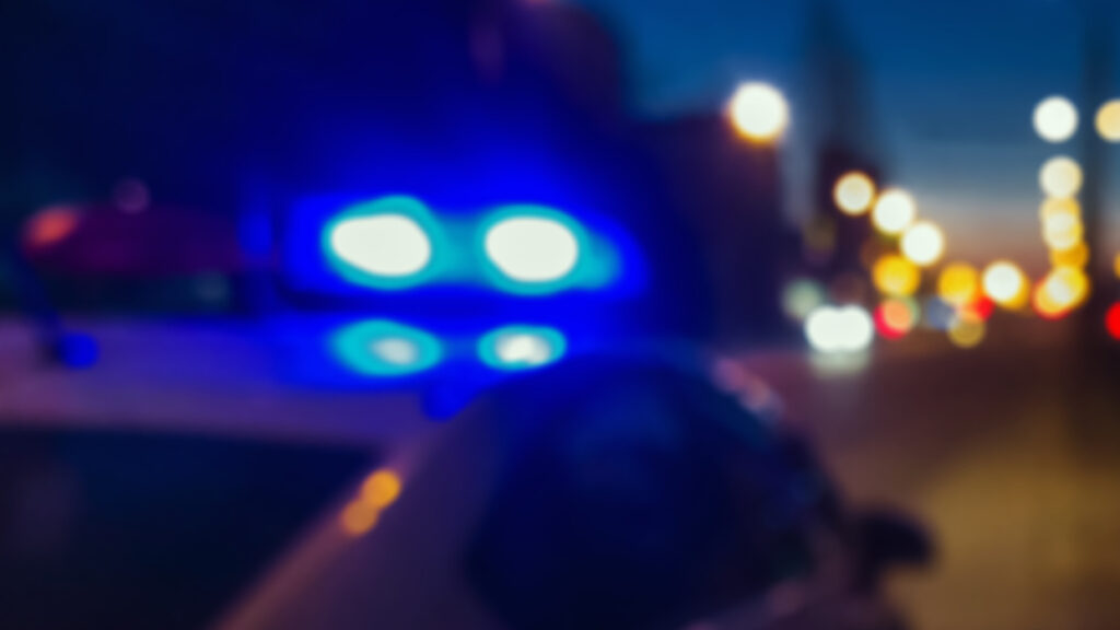 Blurred blue and white police car lights at night with street lights and vehicles in background