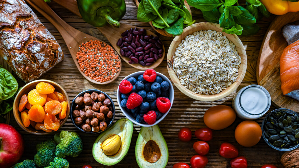 Assortment of fresh vegetables, fruits, grains, nuts, eggs, salmon, and bread arranged on a wooden table