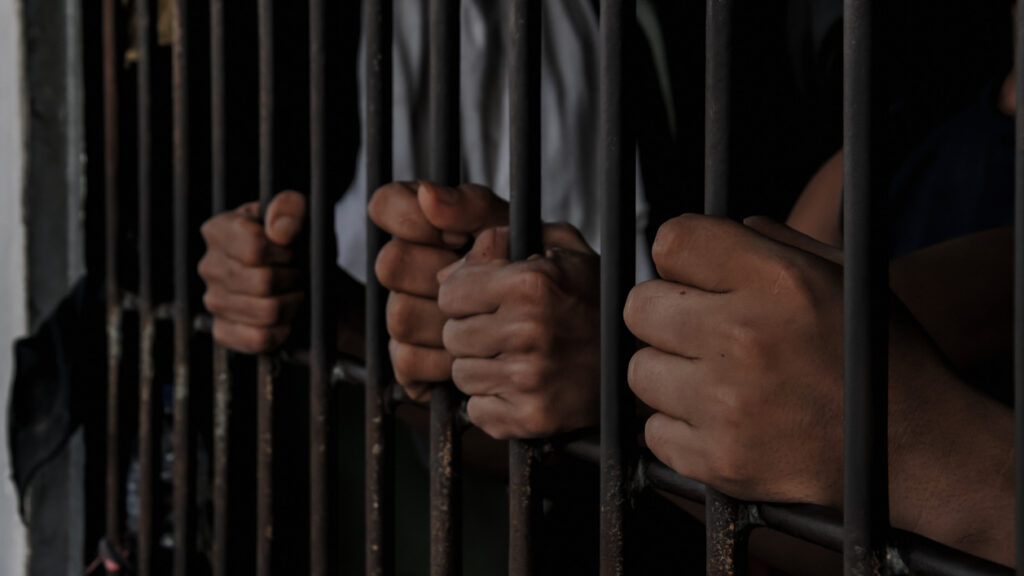 prisoner's hands behind bars with black background
