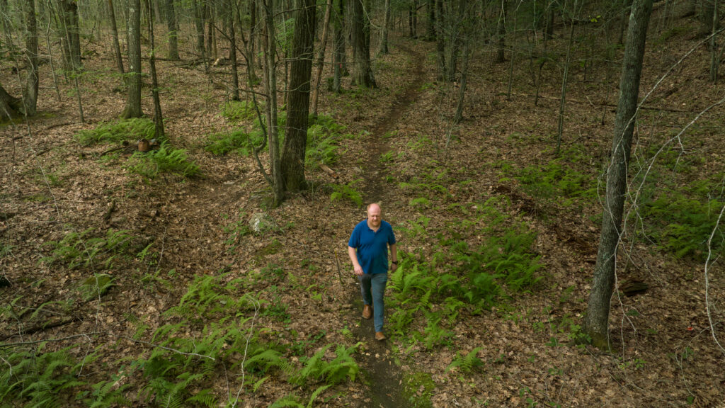 Charles Copley walks a dirt trail through ferns and trees on his Roxbury, Connecticut property