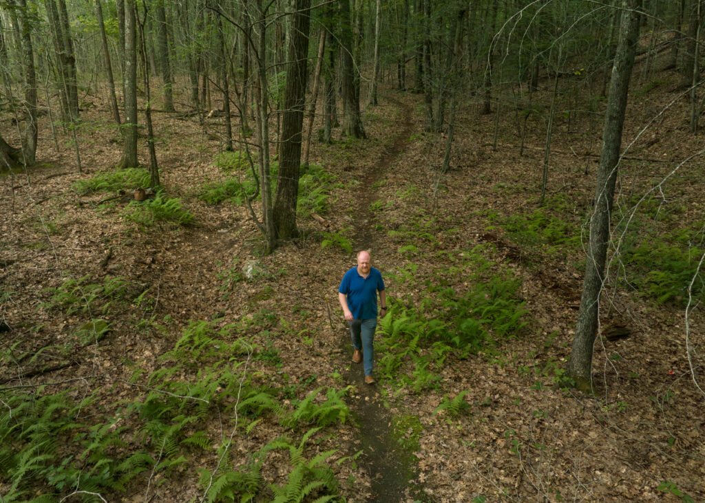 Charles Copley walks a dirt trail through ferns and trees on his Roxbury, Connecticut property