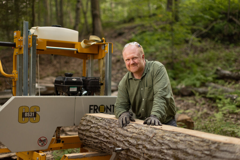 Charles Copley stands beside a portable sawmill with a log on his Roxbury, Connecticut property