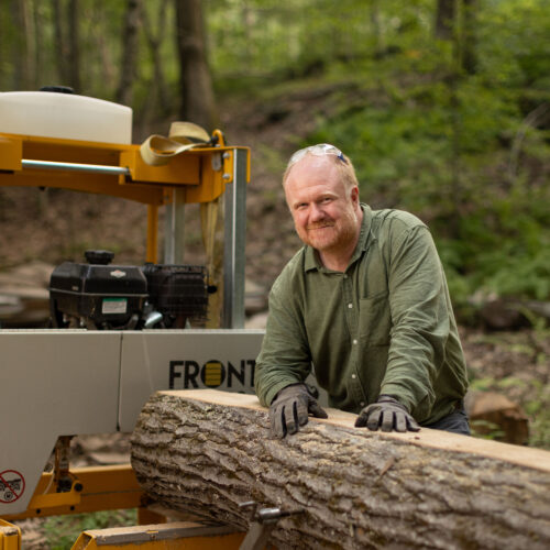 Charles Copley stands beside a portable sawmill with a log on his Roxbury, Connecticut property
