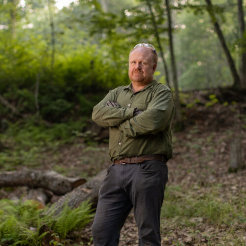 Charles Copley stands arms crossed on his wooded property in Roxbury, Connecticut