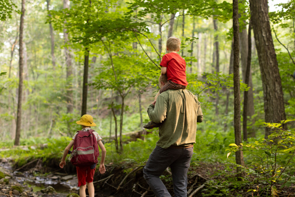 Charles Copley carries his son while hiking a wooded trail with his other child in Roxbury, Connecticut