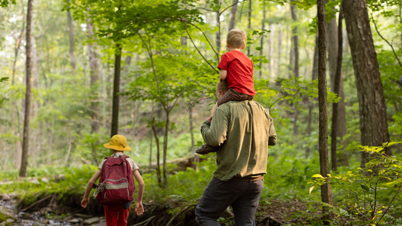 Charles Copley carries his son while hiking a wooded trail with his other child in Roxbury, Connecticut