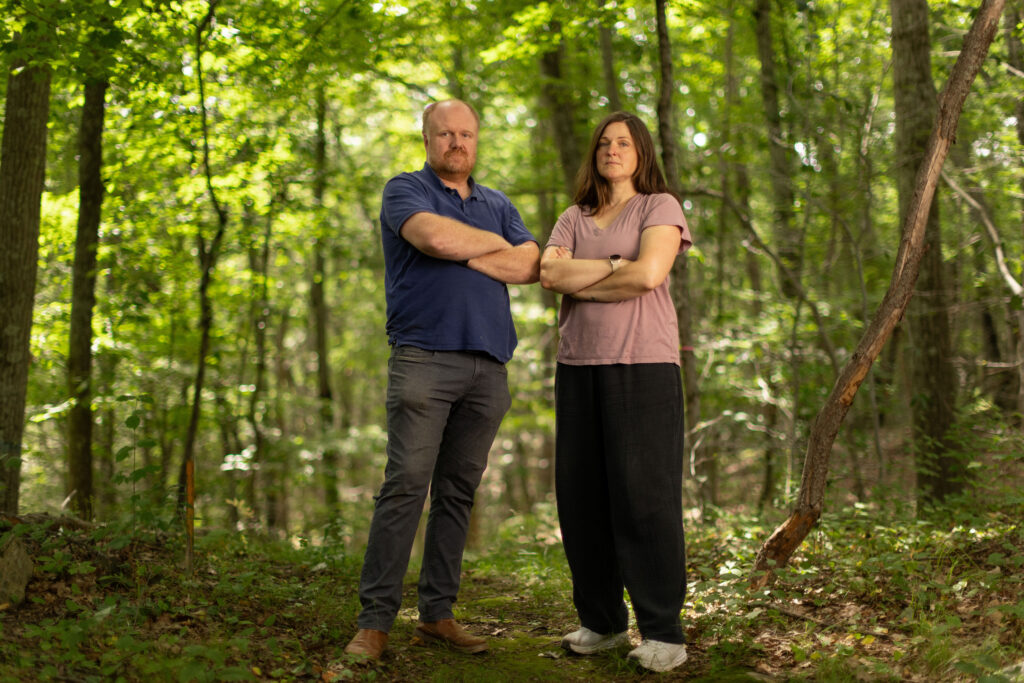 Charles and Eli Copley stand arms crossed on a wooded trail on their Roxbury, Connecticut property.