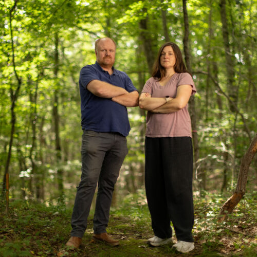Charles and Eli Copley stand arms crossed on a wooded trail on their Roxbury, Connecticut property.