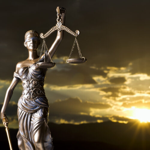 Bronze statue of Lady Justice holding scales and sword against a dramatic sunset sky