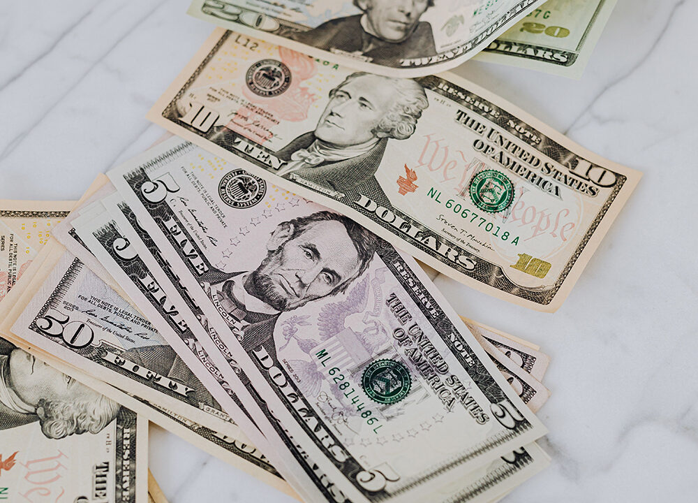 Scattered U.S. currency bills in various denominations on a white marble surface