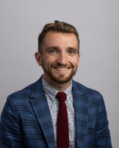 Daniel King smiling in a plaid blazer and maroon tie, professional headshot portrait