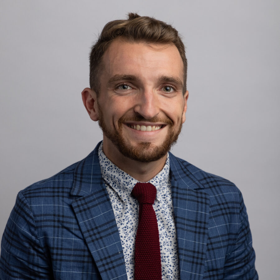 Daniel King smiling in a plaid blazer and maroon tie, professional headshot portrait
