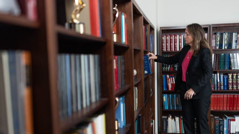 Woman in suit reaching for a book on law office shelves lined with legal volumes