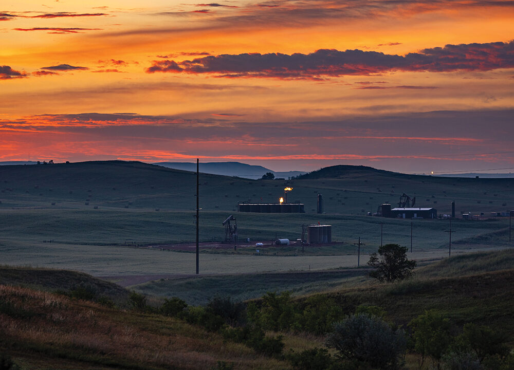 Natural gas drilling facilities and pumpjacks across rolling grasslands at sunset in North Dakota