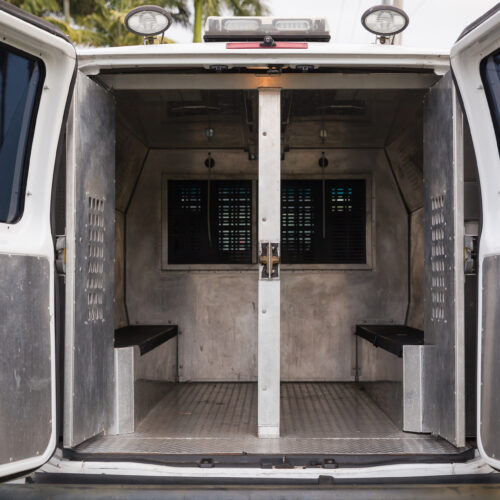 Rear doors open on a police van, showing metal bench seats used for transporting prisoners
