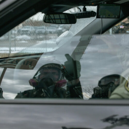 Person wearing a gas mask sits inside a vehicle near law enforcement officers at a protest scene