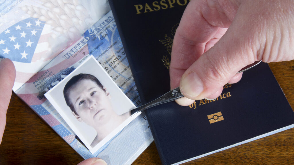 Hand using tweezers to place an ID photo onto a U.S. passport, suggesting document forgery