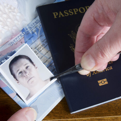 Hand using tweezers to place an ID photo onto a U.S. passport, suggesting document forgery