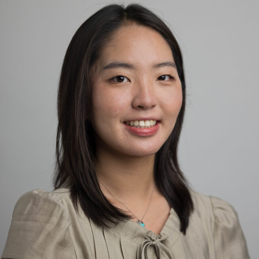 Woman with long dark hair smiling against a light gray background in a professional headshot