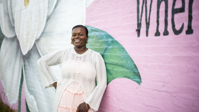 Woman smiling in white sweater, standing before a colorful floral mural