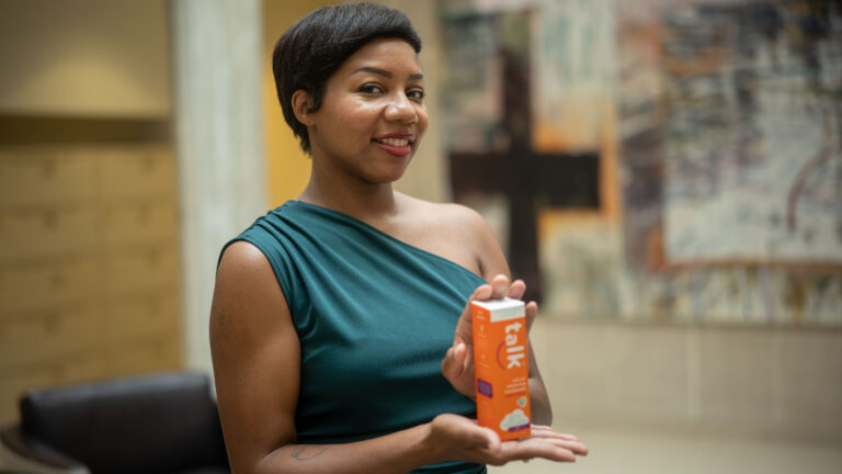 Woman in teal top smiling while holding an orange box of Talk toothpaste