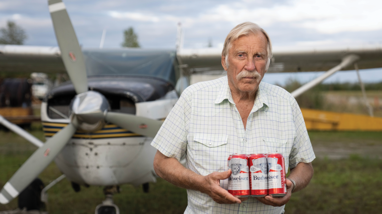 Ken Jouppi holds a six-pack of Budweiser beside his small plane at an Alaska airstrip
