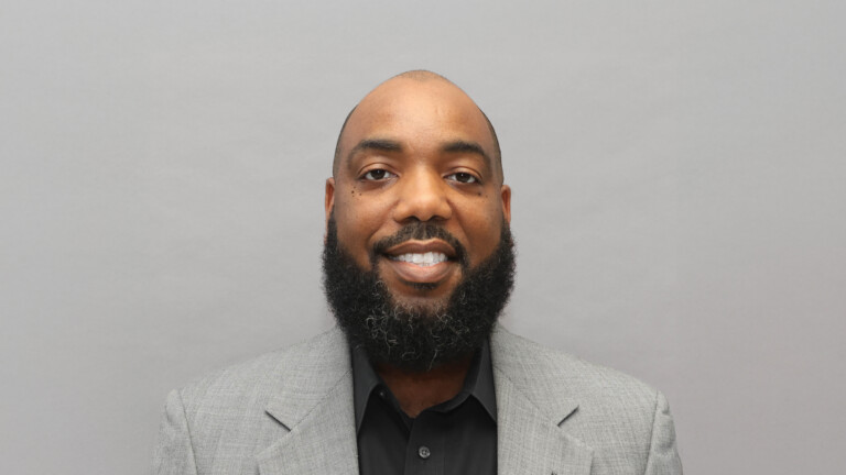 Elliott Hitchcock, bearded man in gray blazer and black shirt, smiling in headshot