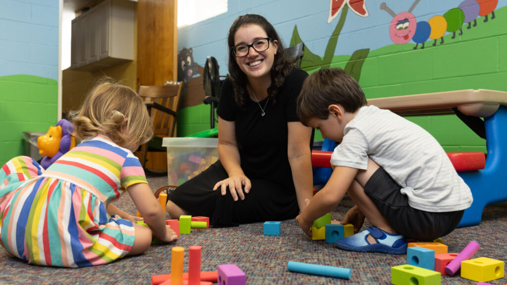 Katy Duckstein sits smiling as two children play with blocks in her Pennsylvania hybrid homeschool classroom