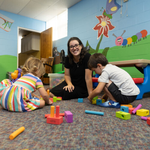 Katy Duckstein sits smiling as two children play with blocks in her Pennsylvania hybrid homeschool classroom